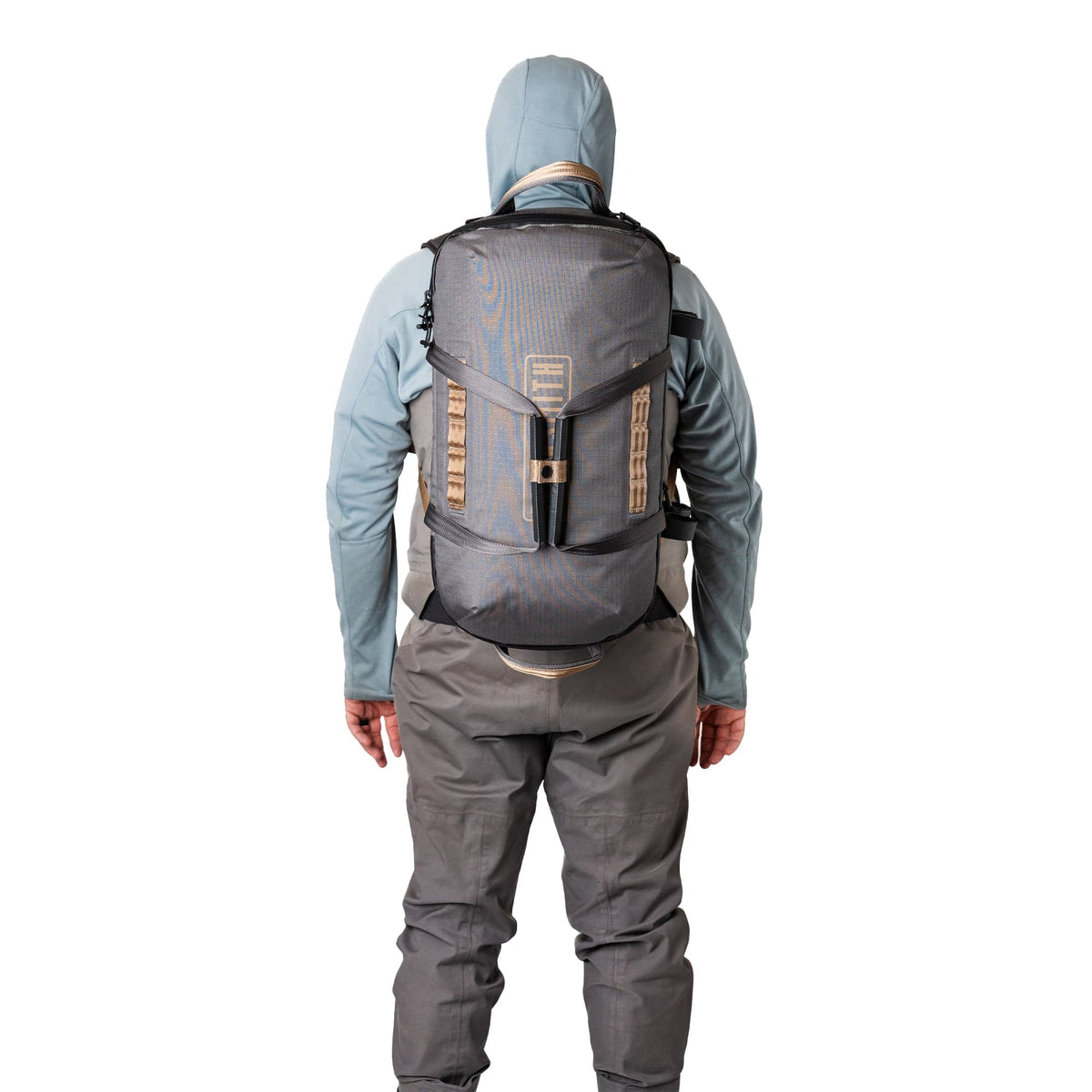 Hiker wearing gray and tan waterproof duffel backpack with hood up against white background