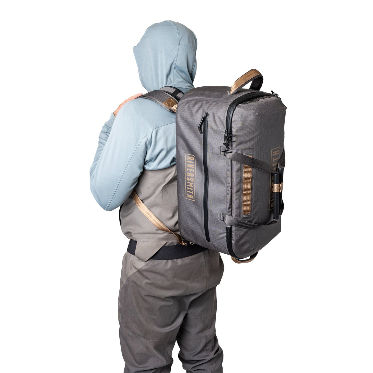 Riversmith waterproof duffel bag in gray with tan leather handles worn by hiker on white background
