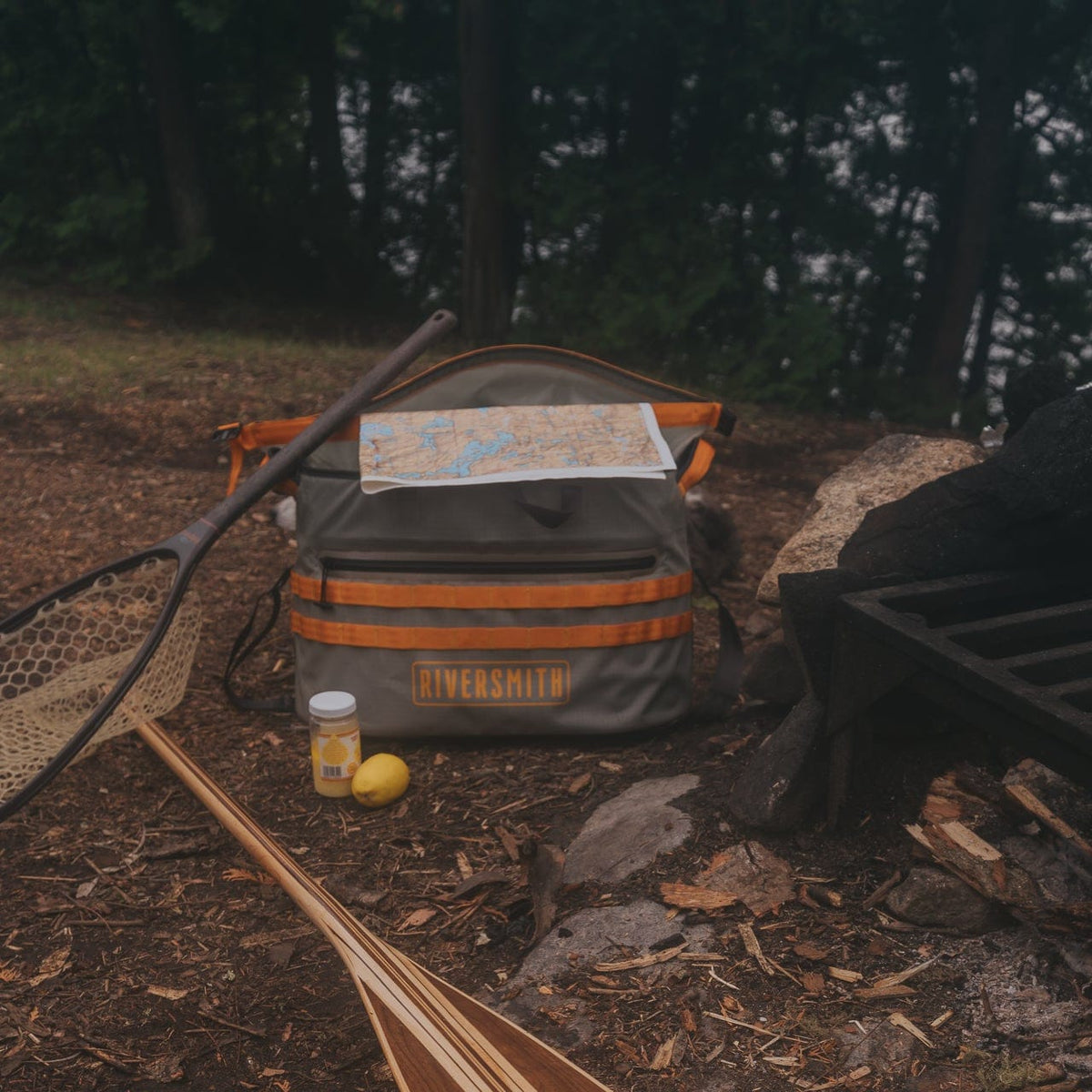 Riversmith The Hauler waterproof tote bag in gray and orange at campsite with fishing gear and map