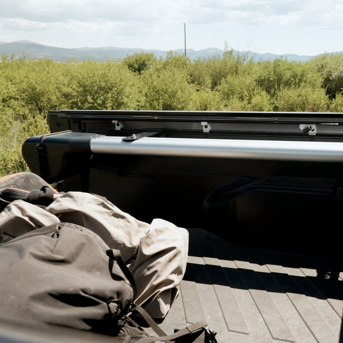 Riversmith truck bed mount rod rack in silver and black installed on pickup truck bed with mountains and trees in background