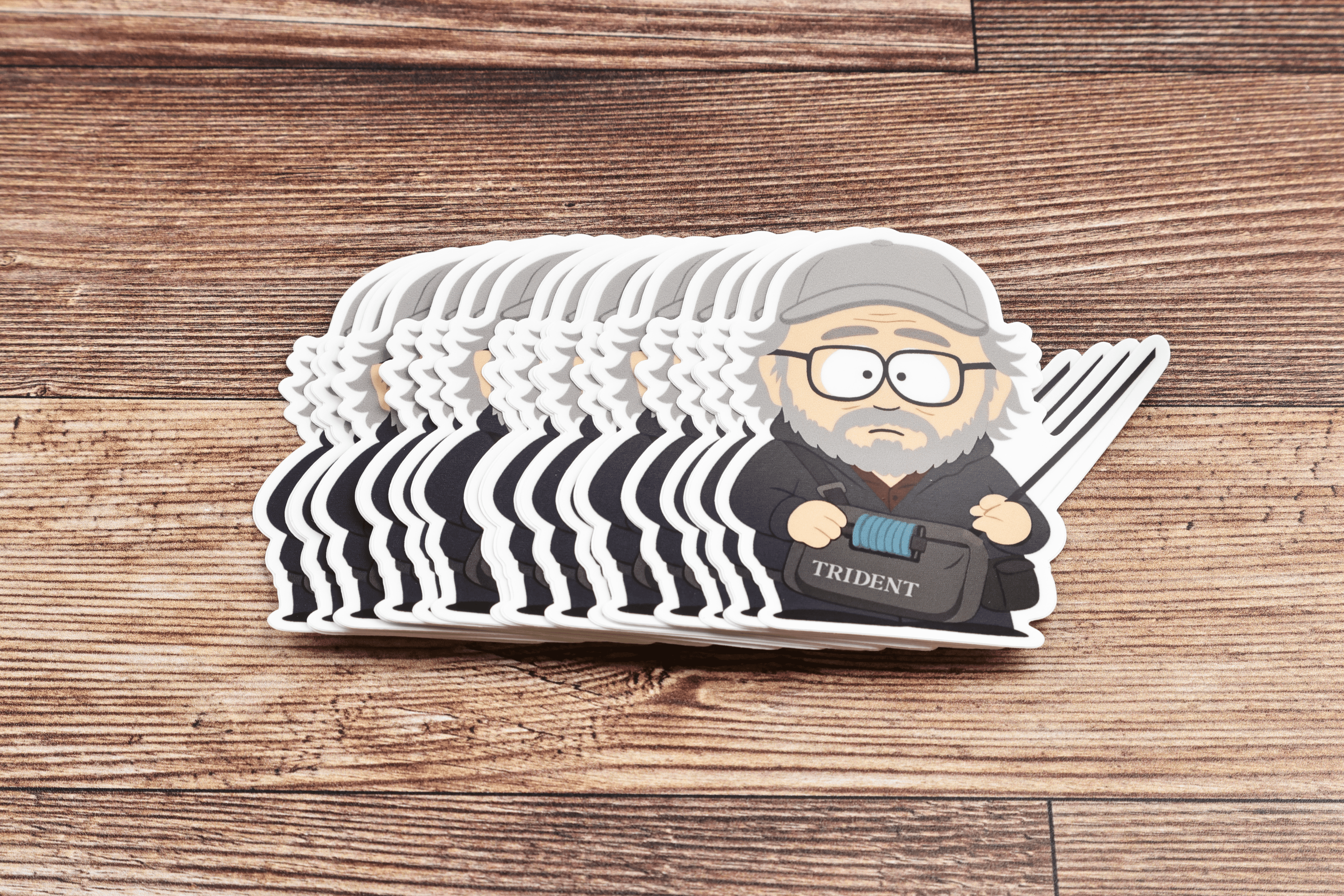 Stack of Trident Rom Rosenbauer vinyl stickers featuring cartoon man with gray beard, cap, glasses on wood background