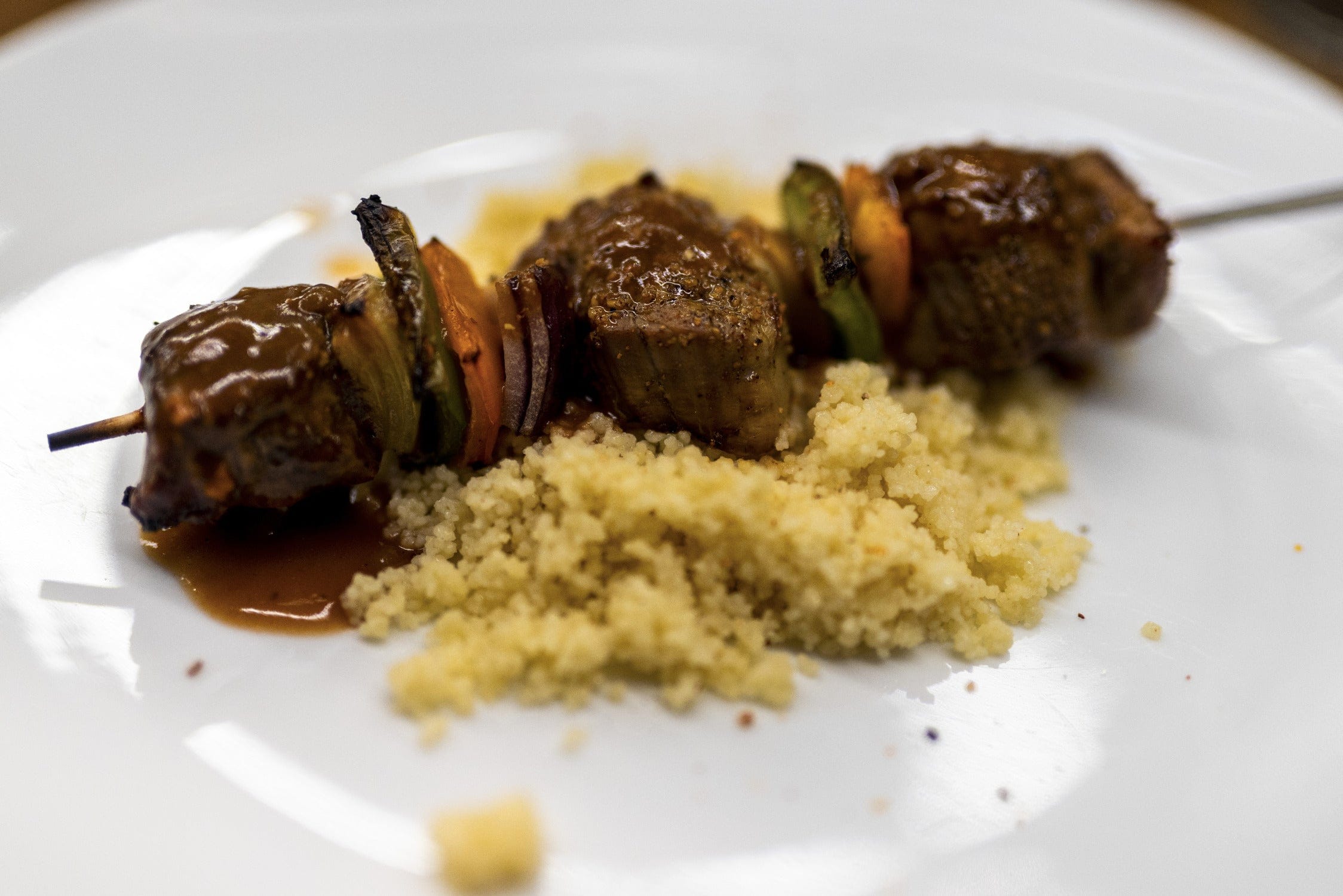 Grilled beef and vegetable skewer with brown sauce on couscous and white plate, Chimehuin Safaris trip dining