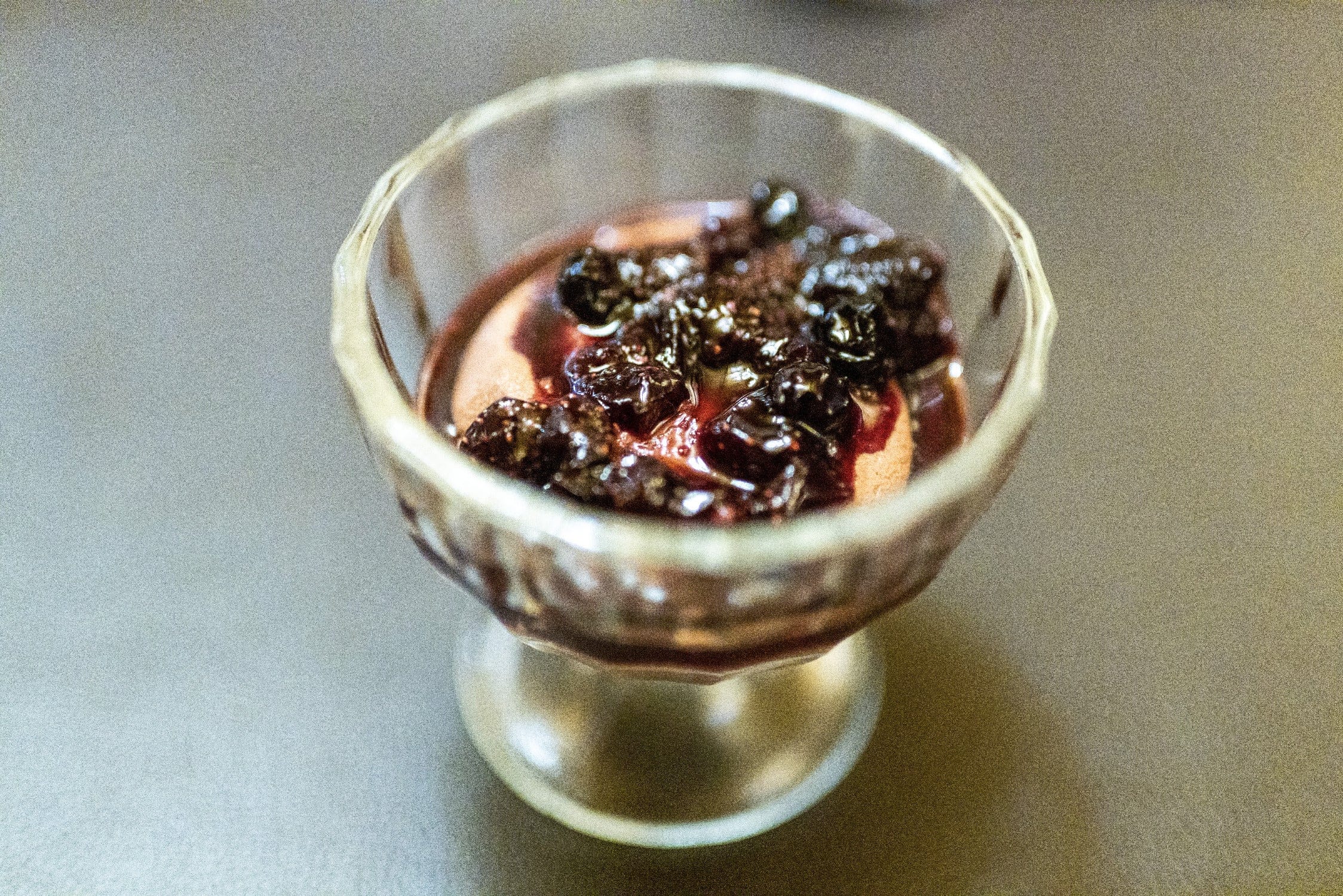 Faceted crystal goblet holding pale cream dessert topped with glossy dark red berry compote, vintage glass style