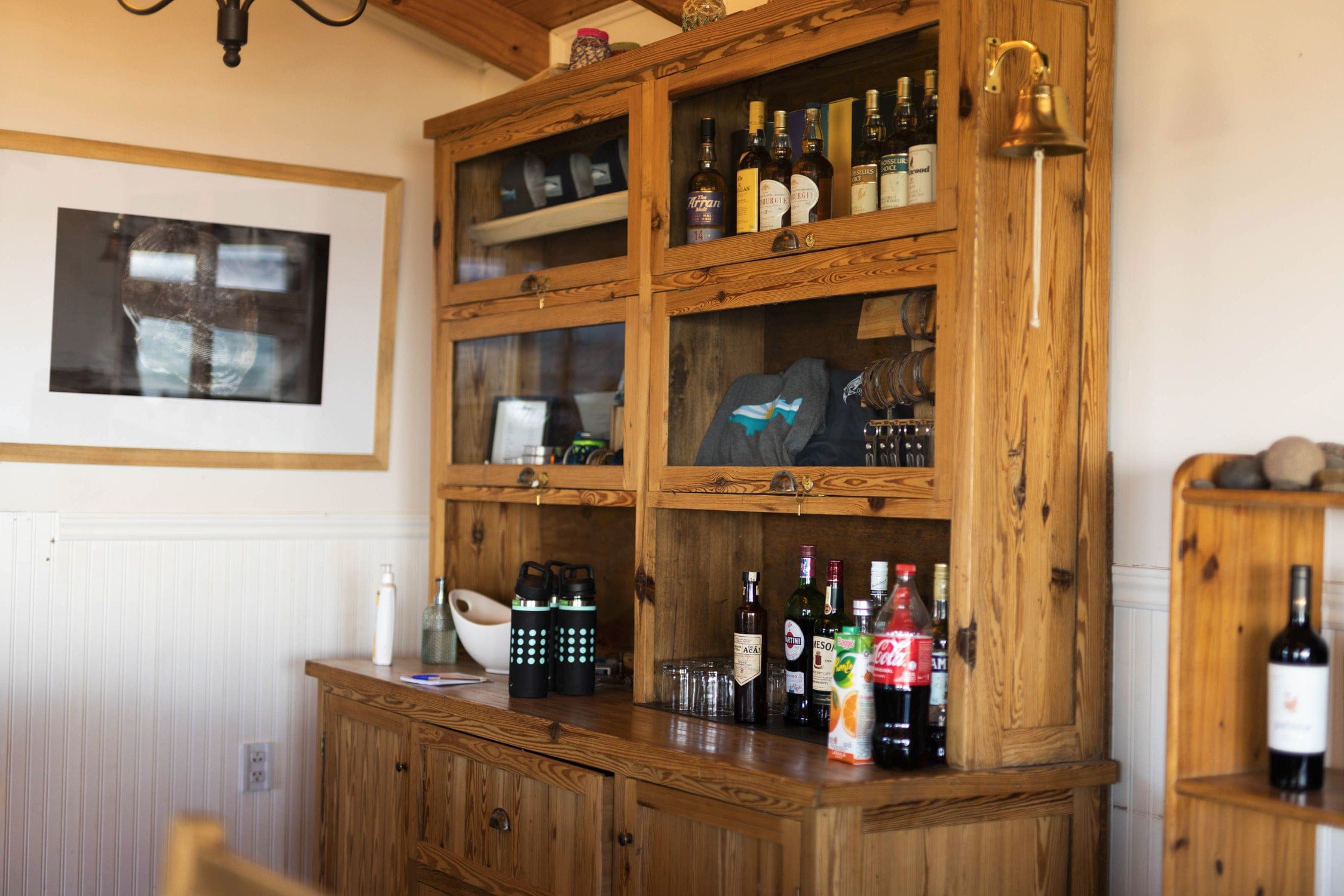 Rustic pine cabinet and counter in lodge reception with glass cubbies holding bottles, folded shirts and a brass bell