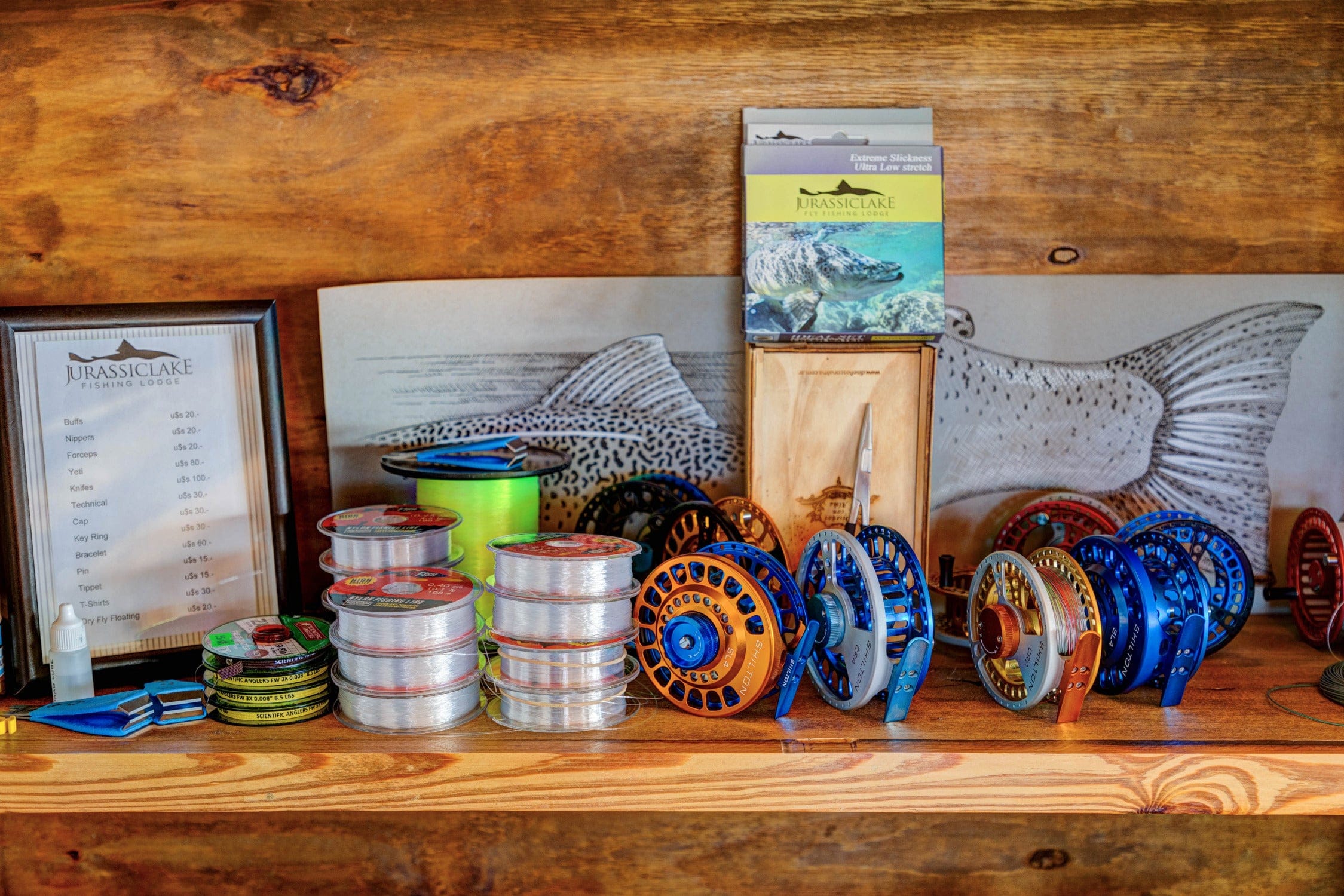 Wooden shelf display with clear fishing line spools and blue/orange anodized fly fishing reels, Jurassic Lake Lodge box