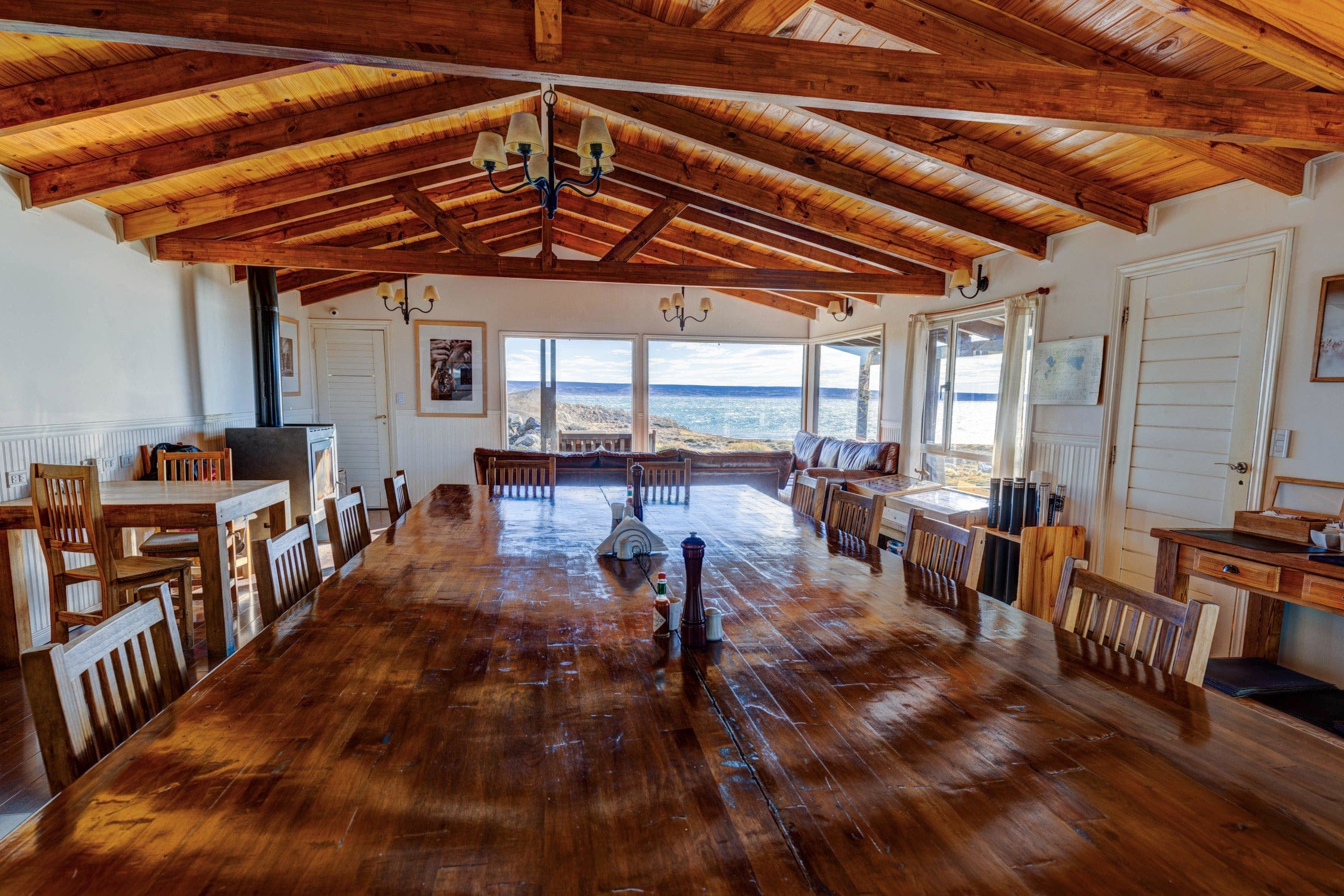 Rustic Trident lodge dining room with long polished dark-wood table, wooden beam ceiling, chandeliers and ocean view windows