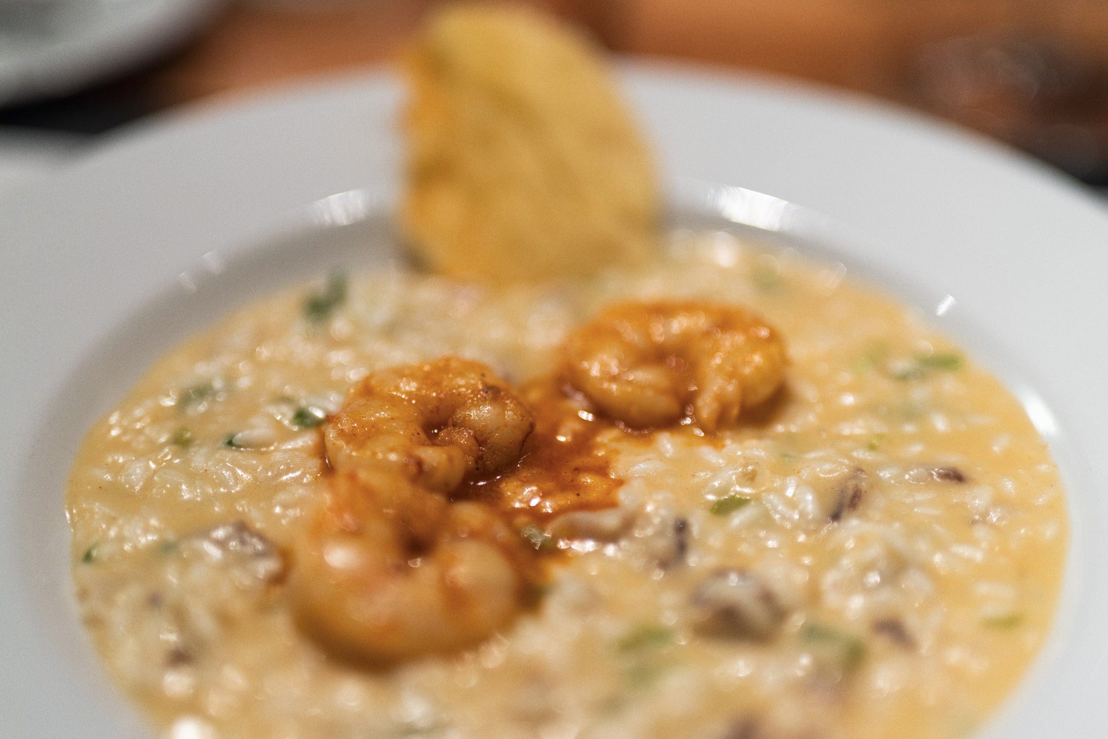 Creamy golden risotto topped with seared shrimp and a crispy toasted crostini on a white plate