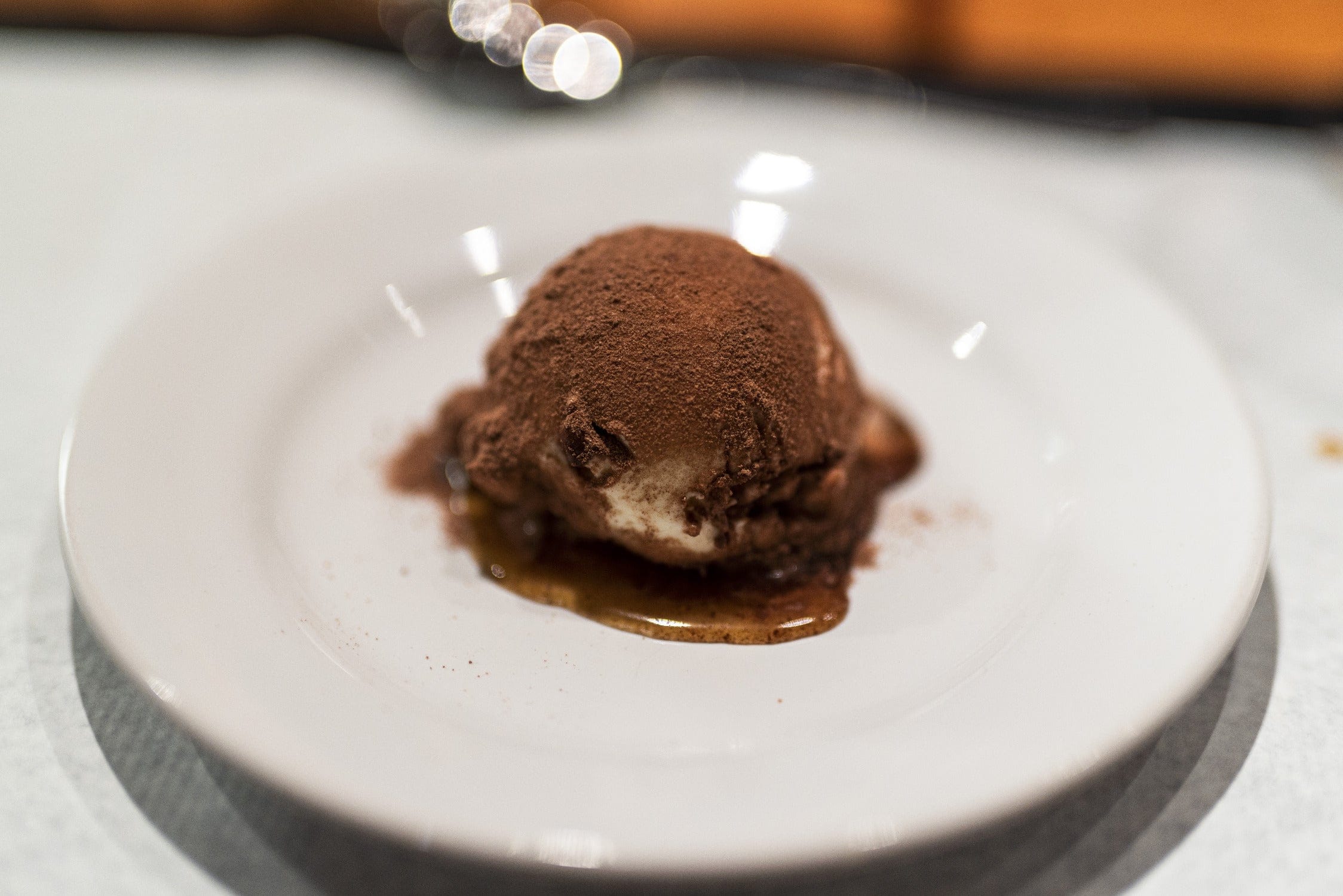 Single chocolate dessert scoop dusted with cocoa powder over caramel sauce on white ceramic plate