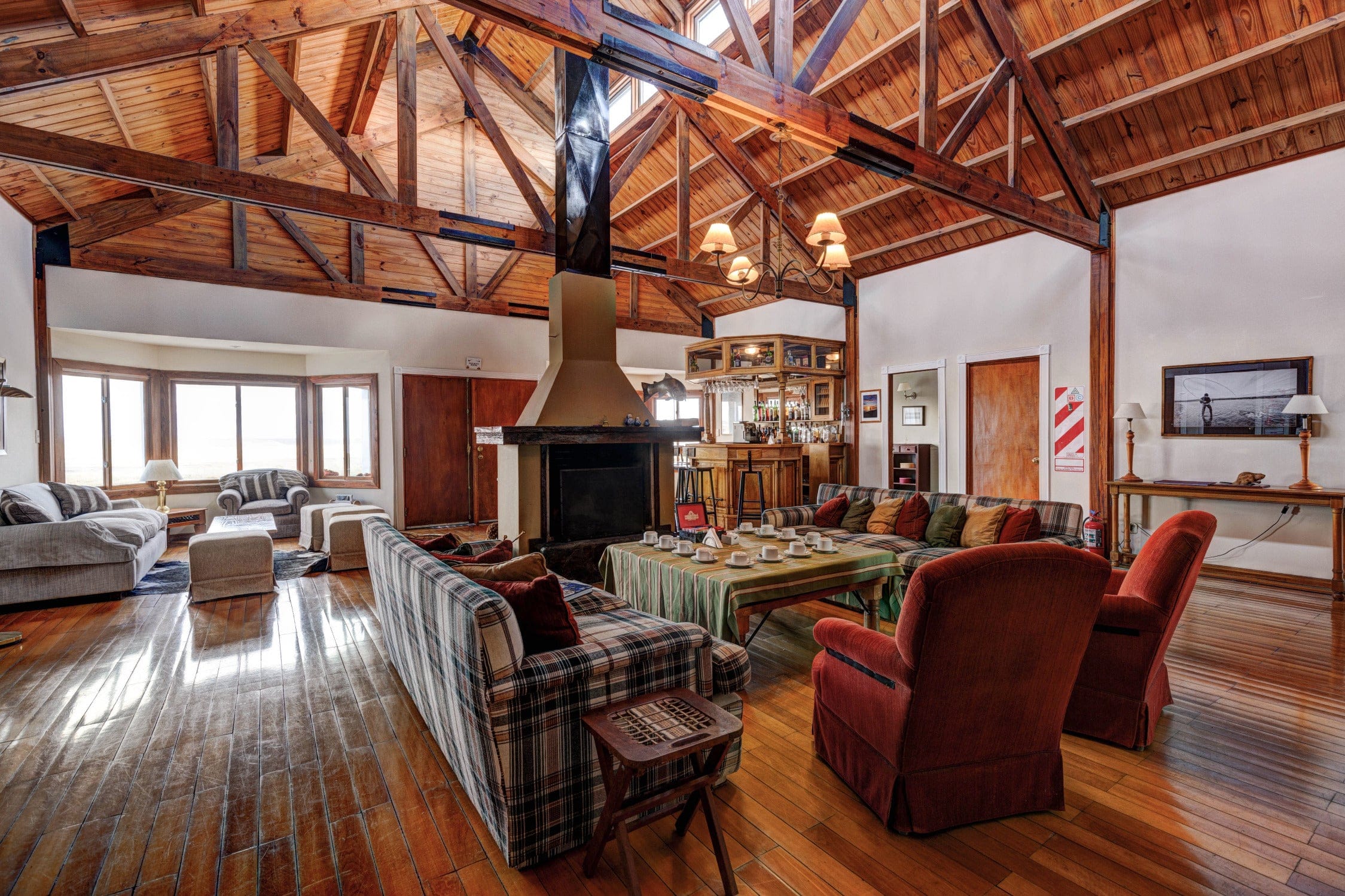 Spacious rustic lodge lounge with exposed wooden beams, central fireplace, plaid sofas and hardwood floors