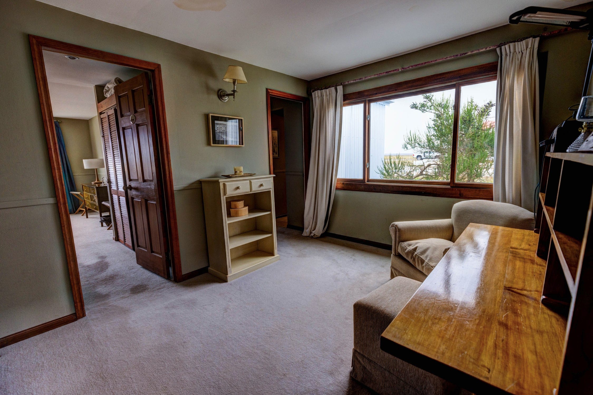Maria Behety Lodge cozy room with olive-green walls, wooden trim and desk, cream curtains and beige armchair