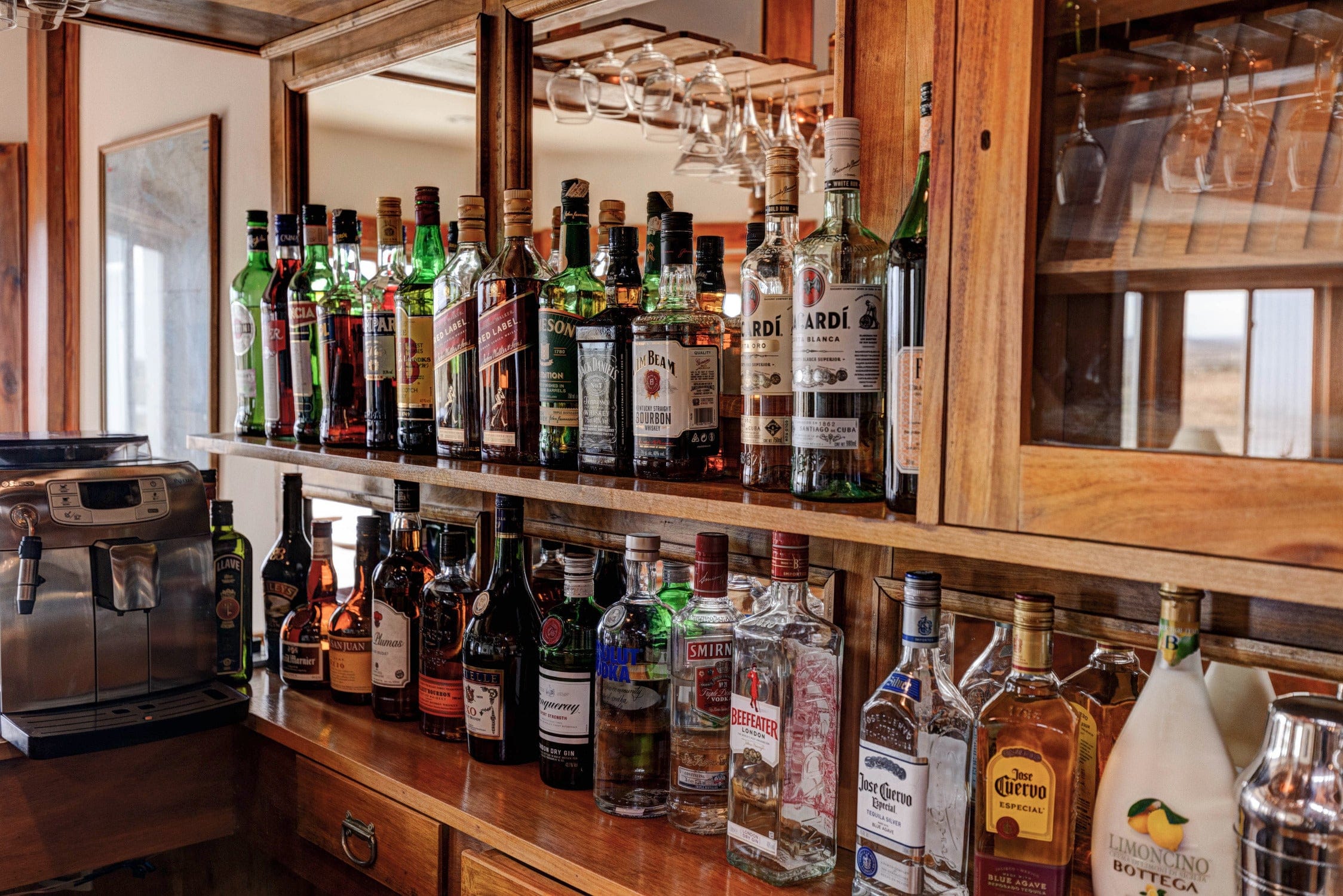 Warm wooden lodge bar with green and amber liquor bottles on shelves, hanging wine glasses and stainless espresso machine