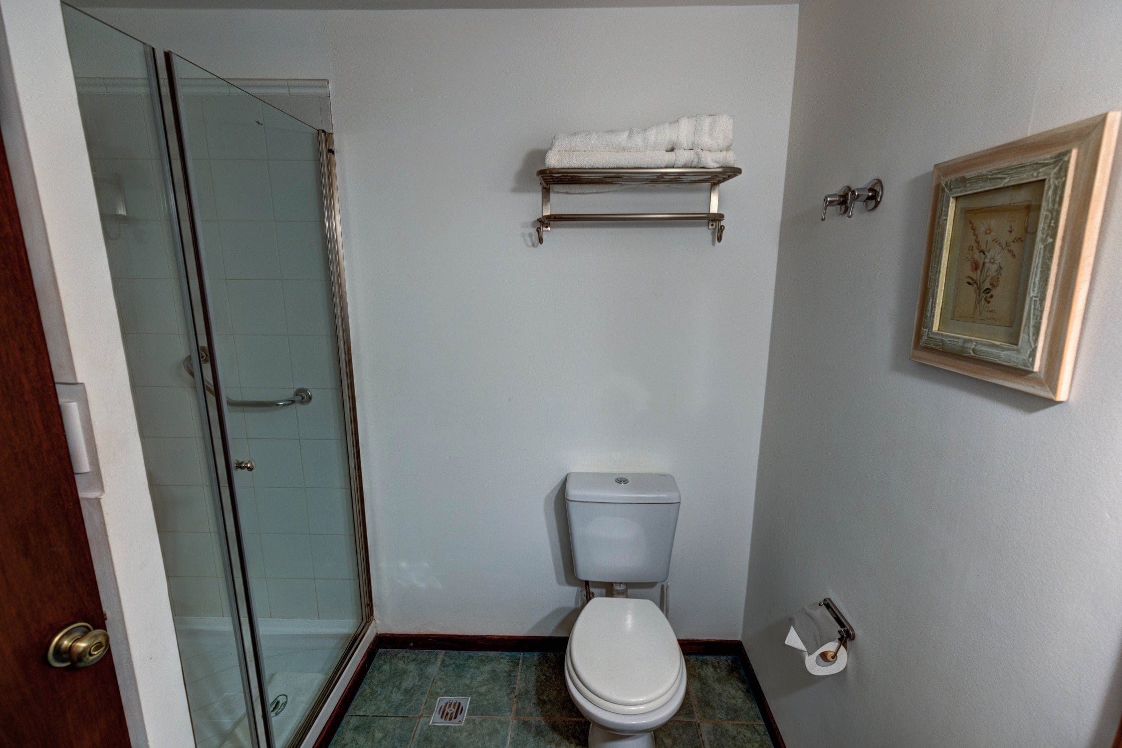 Compact white bathroom with porcelain toilet, glass shower door with chrome frame, metal towel rack and folded white towels