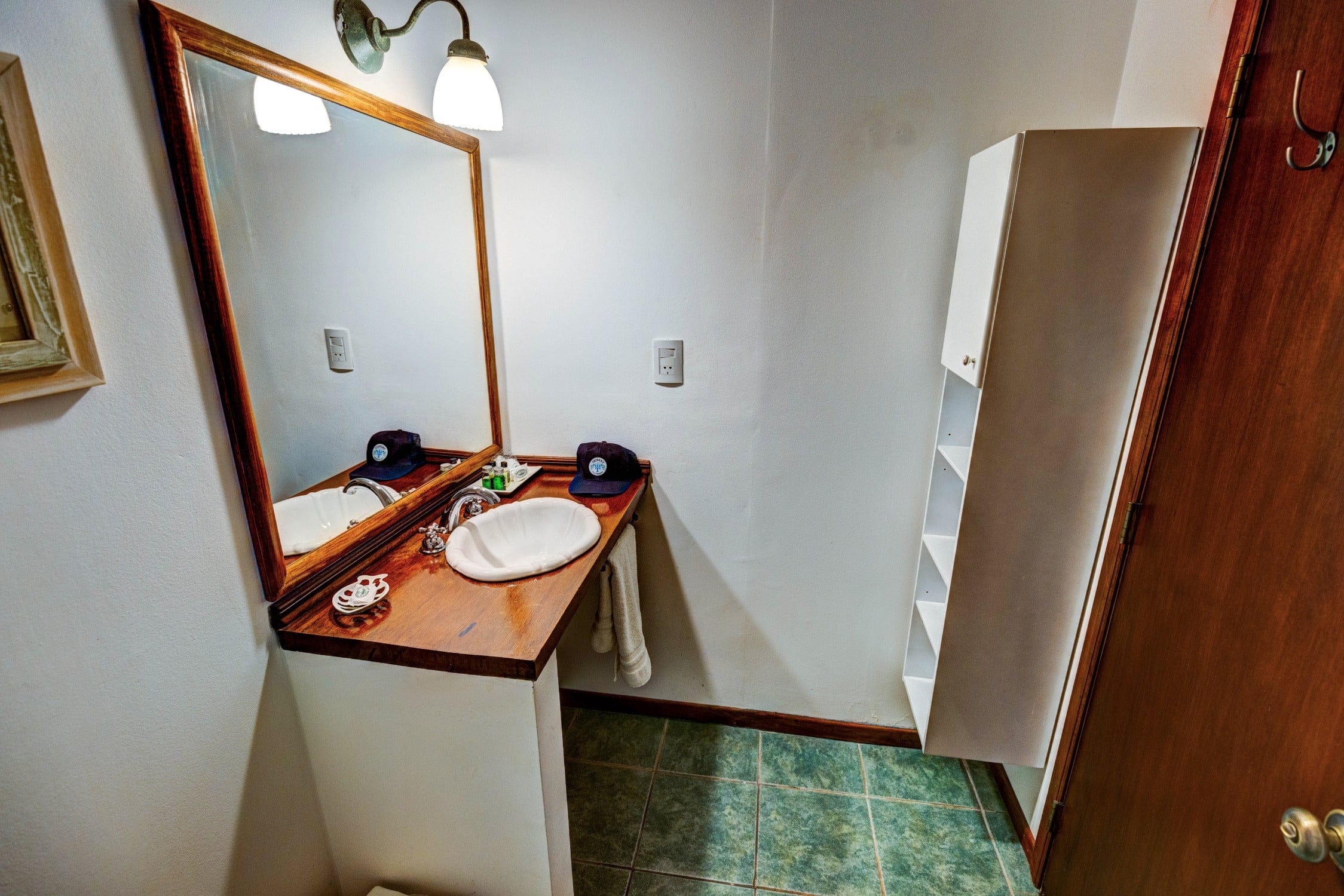 Maria Behety Lodge bathroom vanity with wood countertop, white scalloped sink, framed mirror and green tile floor