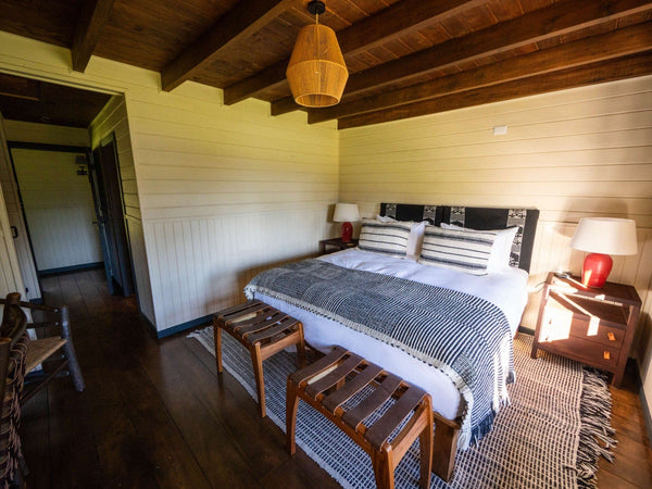 Rustic lodge bedroom with wooden beam ceiling, white shiplap walls, king bed with striped bedding and rattan lamp