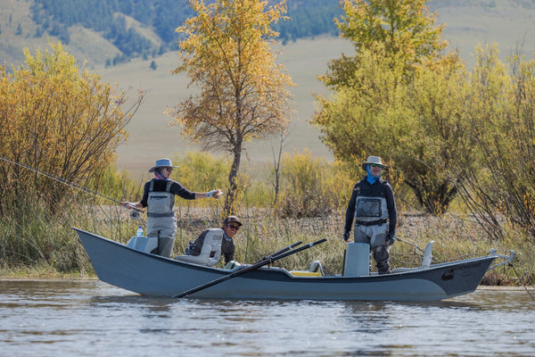 Three anglers in gray aluminum boat wearing chest waders and hats fly-fishing on river with golden trees, expedition