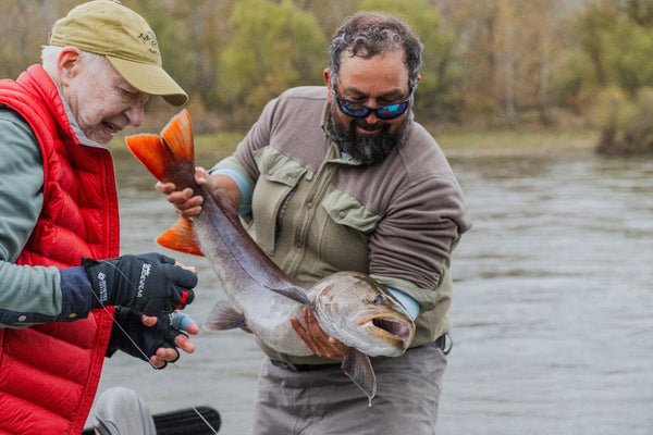 Two anglers holding a large orange‑tailed salmon on a river during a Trident MRO Combination fishing trip
