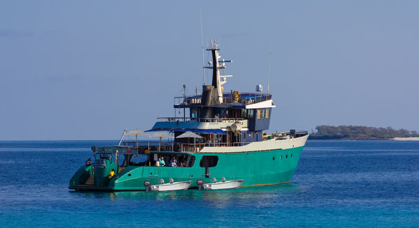 Teal-hulled Trident Providence Atoll expedition yacht with white superstructure, tenders and shaded decks on clear blue water