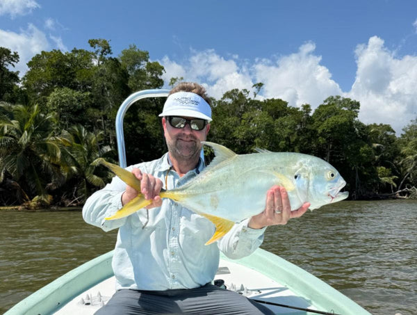 Angler displays golden permit fish catch on shallow-water flats fishing boat in Belize